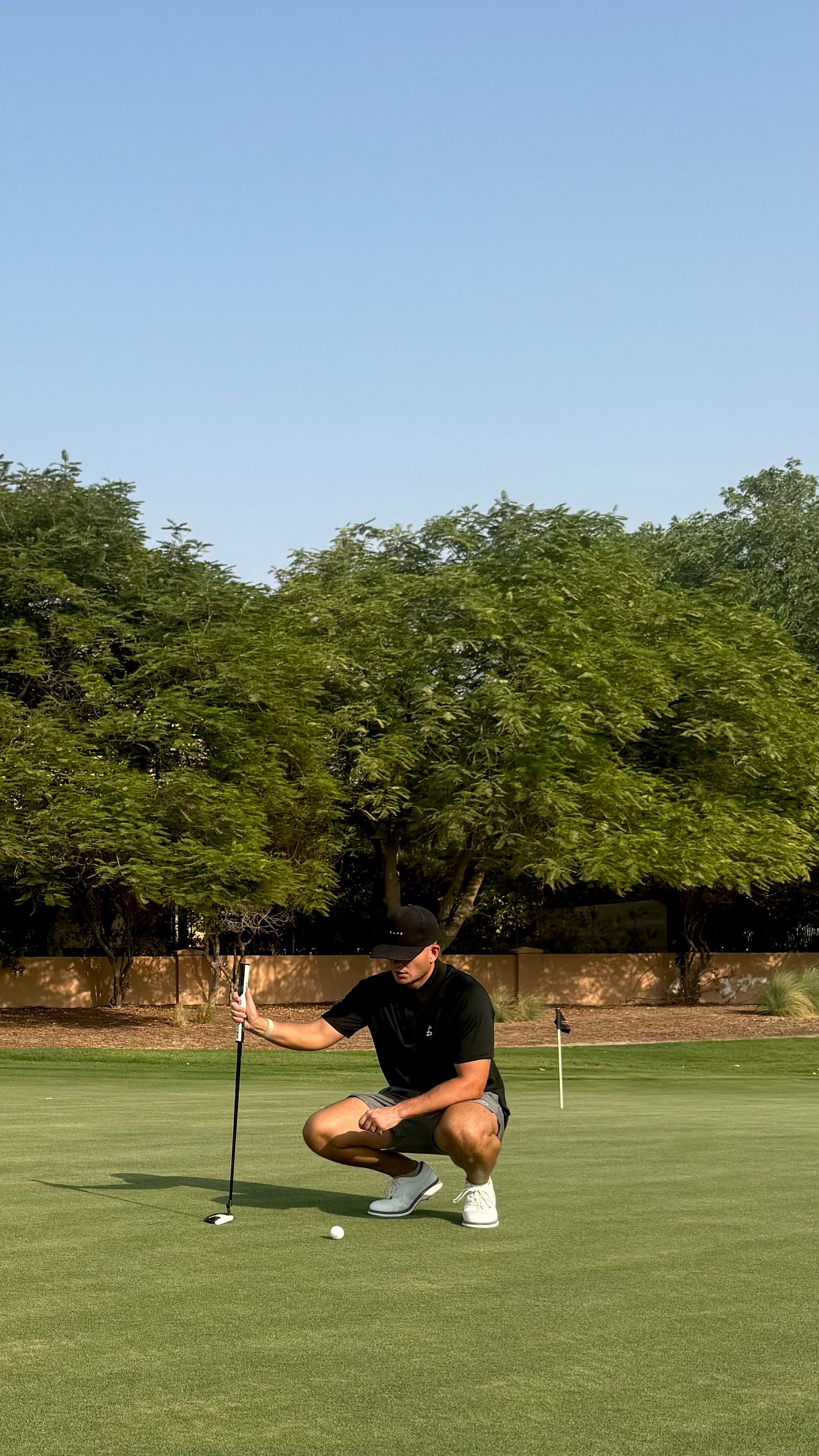 Golfer wearing a black DUNE polo and cap reading a putt in Dubai